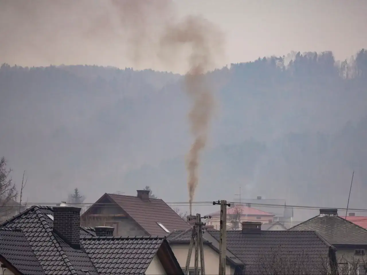 Dym z komina unosi się w szare, mgliste powietrze, tworząc widok typowy dla problemu, jakim jest co to jest smog.
