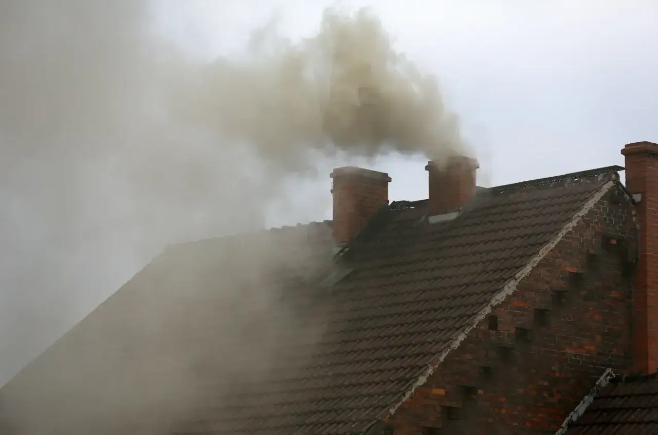 Gęsty dym wydobywa się z ceglanych kominów na dachu. To właśnie co to jest smog, który zatruwa powietrze.